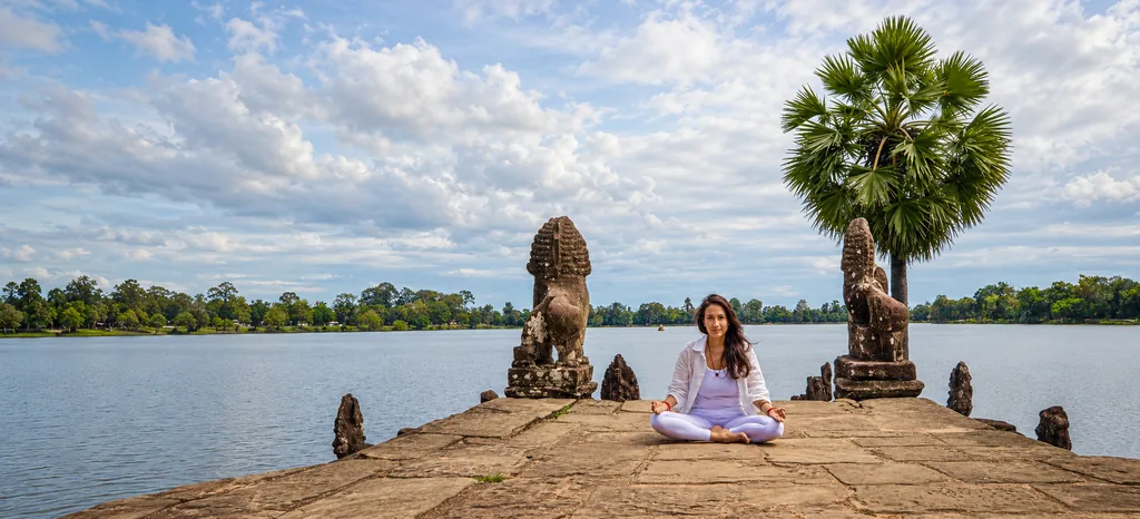 Marielisa Padilla seated in a lotus posture on the Srah Srang terrace at dawn, sugar palm above, lake behind